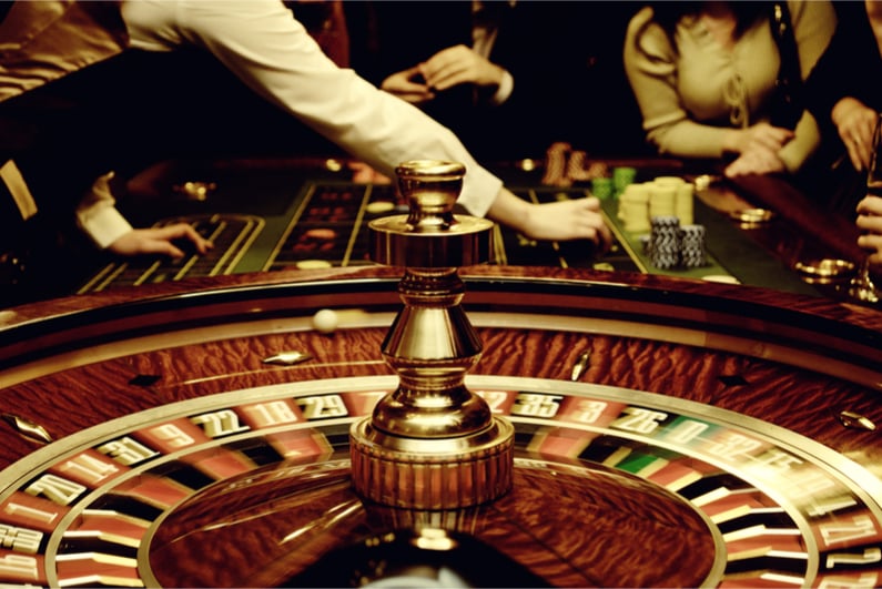 People play casino games: gold spinning roulette with motion of players, croupier (dealer) and roulette in a modern casino