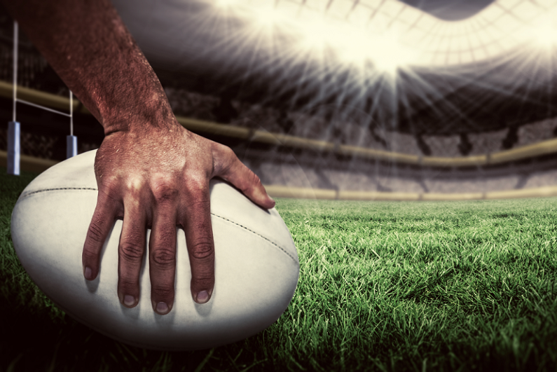 Closeup of a rugby player placing a ball down on the pitch.