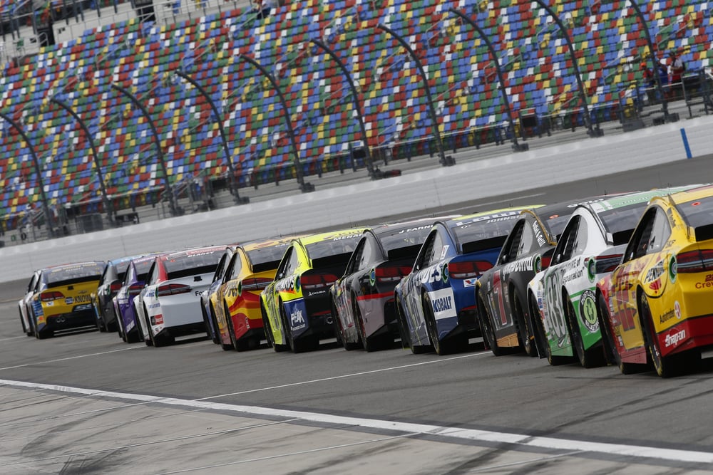 NASCAR cars on a racetrack with audience watching on