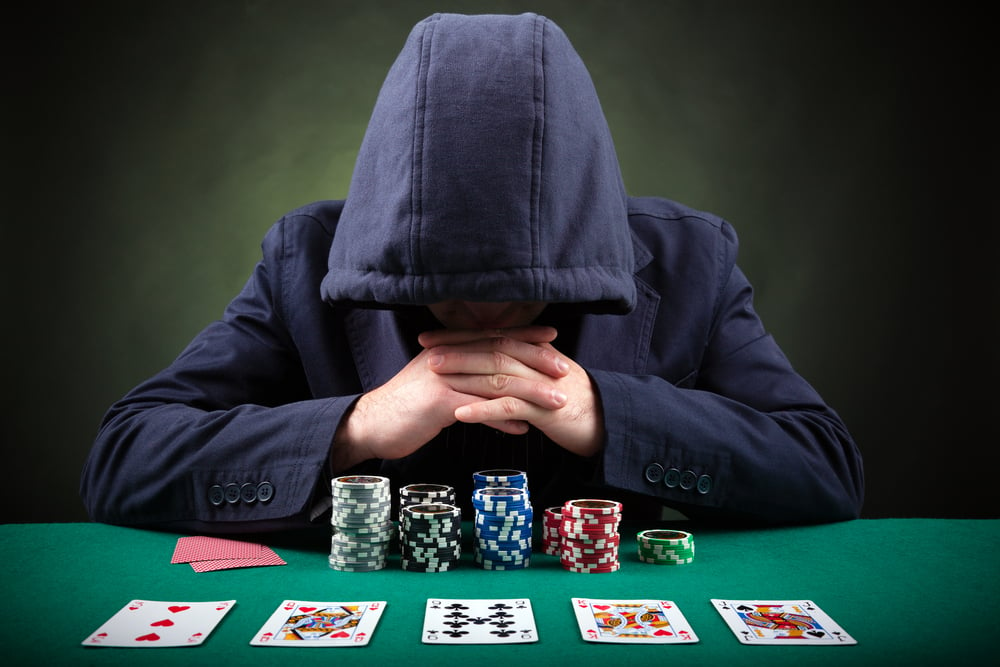 hooded poker player sitting at poker table with cards and chips