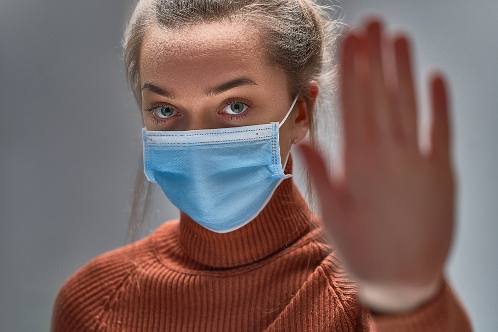 blonde woman wearing face mask puts up hand gesturing a stop sign