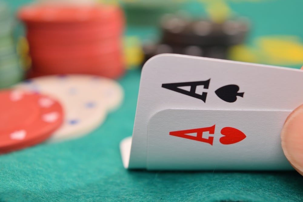 poker player holding two Ace cards against green felt and poker chips backdrop